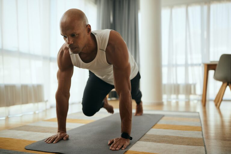 Young African American athletic man doing running plank exercise while working out at home.
