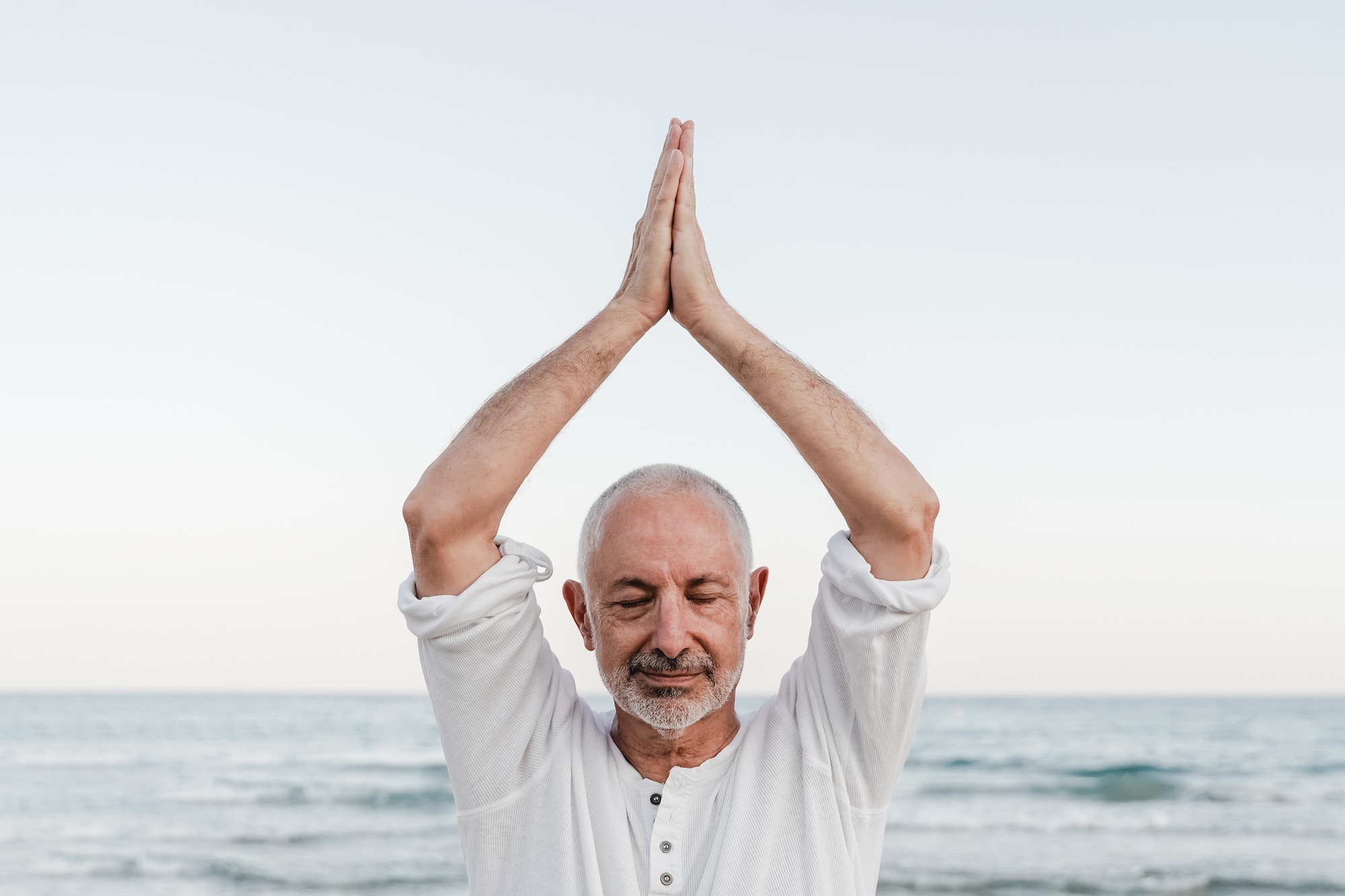 Senior man doing yoga meditation outdoor at the beach - Elderly and healthy lifestyle