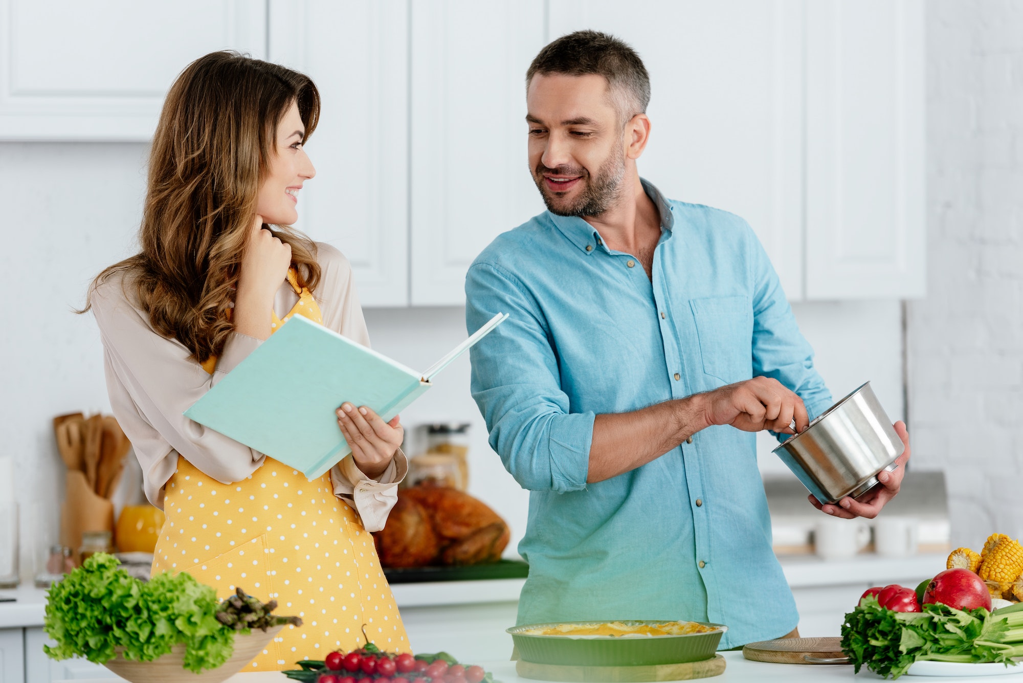 smiling couple reading recipe book while cooking together at kitchen
