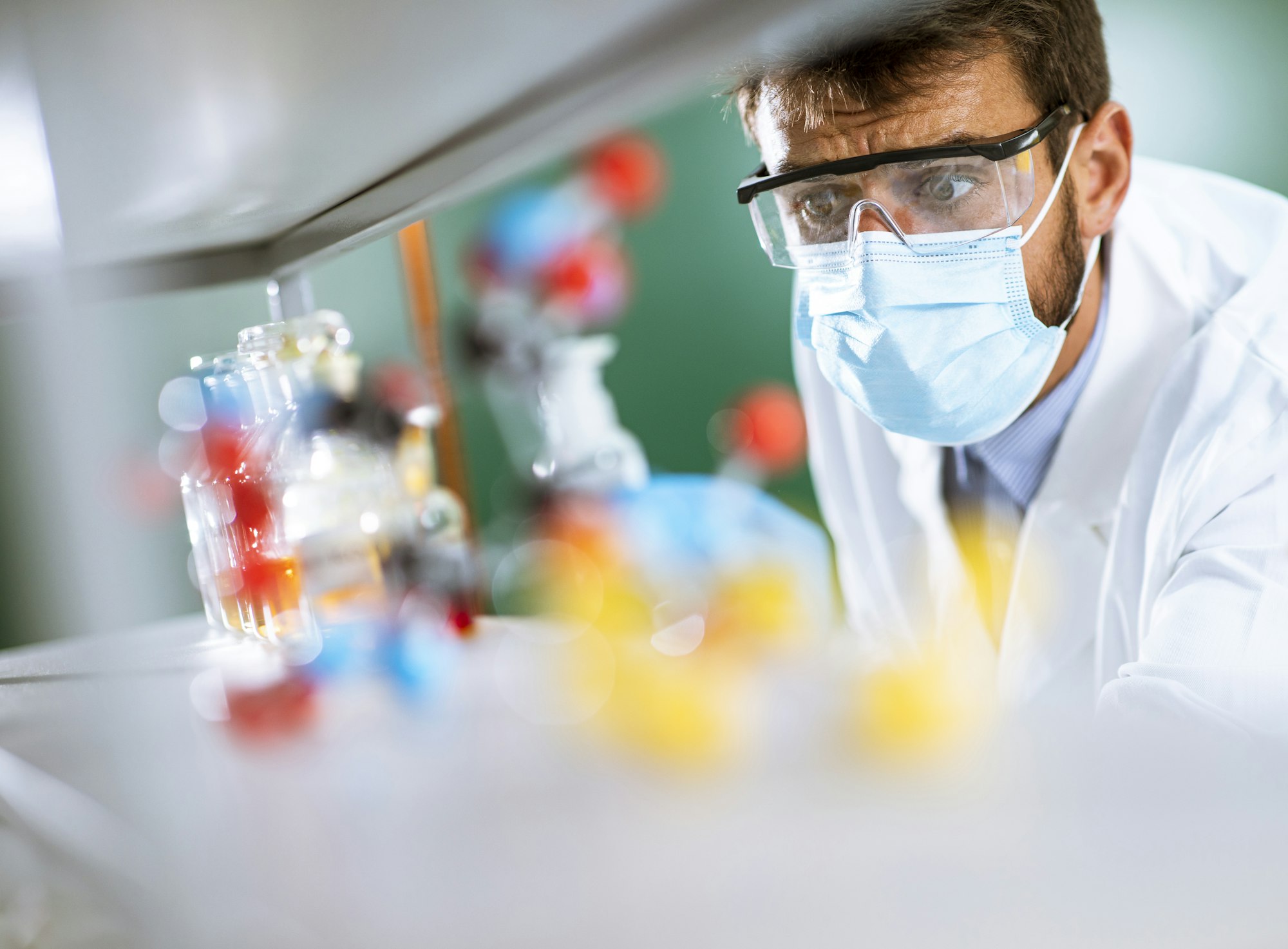 Young researcher with protective goggles checking test tubes